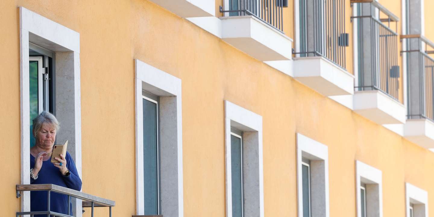 Uma mulher consulta o telemóvel à janela de um prédio, em Lisboa, 06 de agosto de 2024. Habitação. Casas. Imobiliário. ANTÓNIO PEDRO SANTOS/LUSA