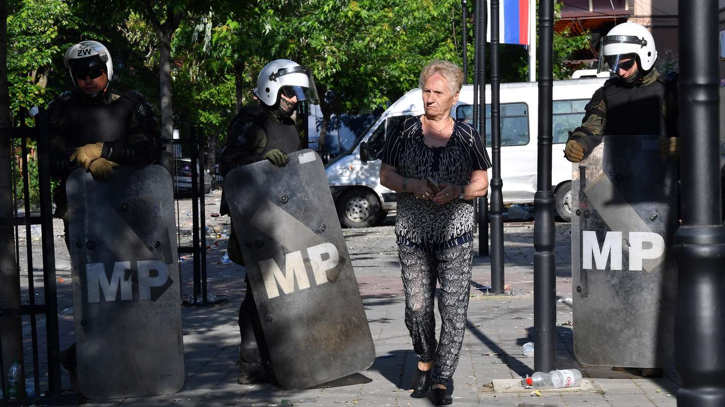 epa10662724 A woman walks past soldiers of NATO-led international peacekeeping Kosovo Force (KFOR) as they set up positions in front of the building of the municipality in Zvecan, Kosovo, 30 May 2023. At least 25 KFOR peacekeepers and 53 civilians were injured after clashes between security forces and ethnic Serbs broke out in Zvecan on 30 May 2023. Tensions continue in northern Kosovo’s region, with a majority of ethnic Serbian people, which arose after ethnic Albanians mayors took offices in four towns following elections boycotted by the Serbian community.  EPA/GEORGI LICOVSKI