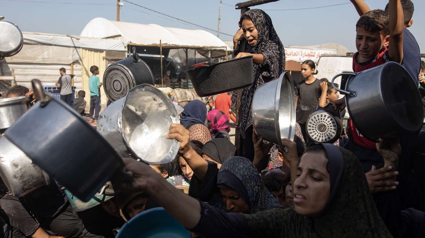 epa12495146 Displaced Palestinians, including children, hold metal pots and pans as they gather to receive food from a charity kitchen in Khan Yunis, southern Gaza Strip, 31 October 2025, amid a ceasefire between Israel and Hamas.  EPA/HAITHAM IMAD