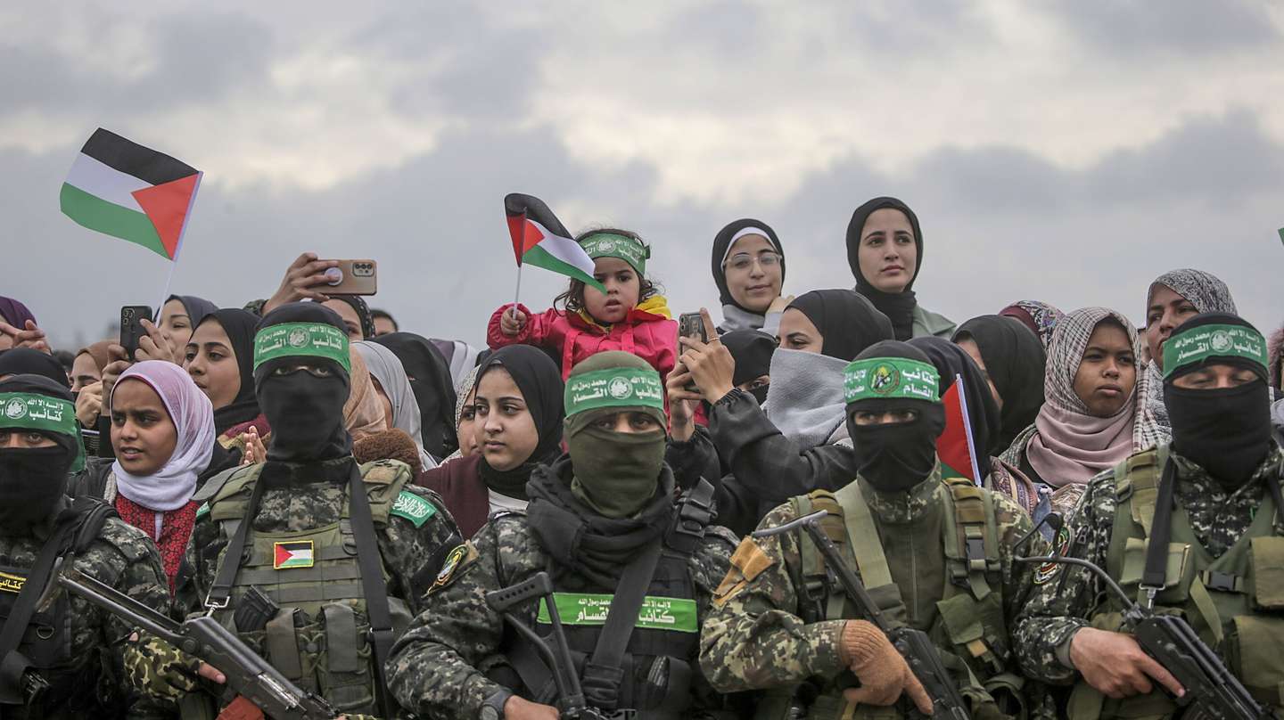 epa11915734 Palestinians (rear) stand behind armed fighters from Hamas' Izz ad-Din al-Qassam Brigades during the handover of three Israeli hostages to Red Cross representatives in Al Nuseirat refugee camp, central Gaza Strip, 22 February 2025. Six Israeli hostages were released on 22 February -- three in Nuseirat, two in Rafah and one in Gaza City -- after Hamas handed them over to the Red Cross in Gaza as part of the first phase of the Israel-Hamas ceasefire deal.  EPA/MOHAMMED SABER