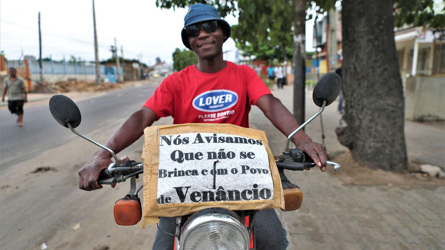 Um apoiante de Venâncio Mondlane mostra um cartaz que transporta na siua motorizada em Maputo, Moçambique, 24 de dezembro de 2024. Um cenário de caos, barricadas, destruição e saques marca hoje a cidade de Maputo, um dia depois da proclamação dos resultados das eleições gerais, mas no meio das mesmas avenidas, bloqueadas por manifestantes, também se cozinha arroz com repolho. LUÍSA NHANTUMBO/LUSA