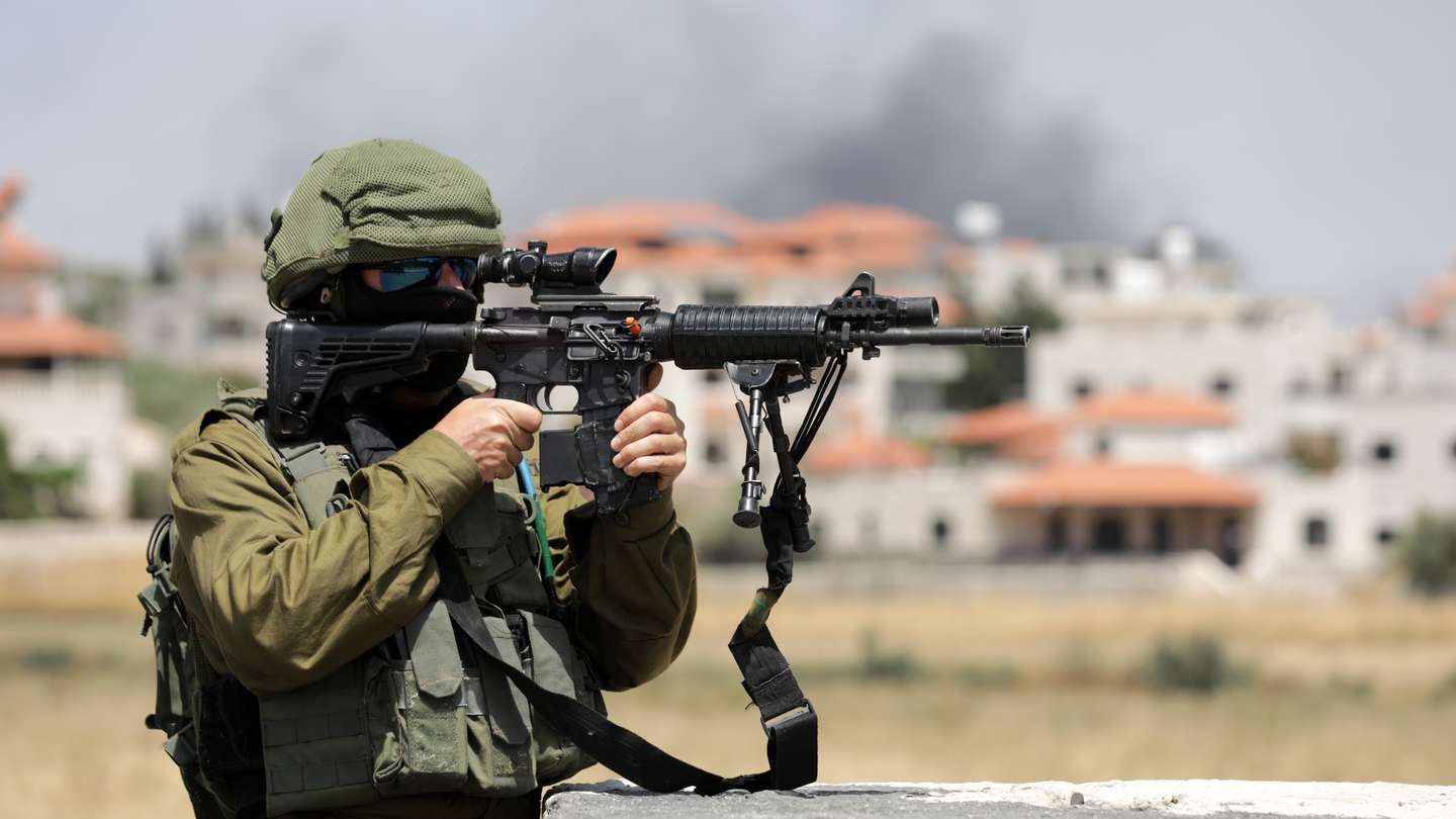 epa10703679 An Israeli soldier stands guard as smoke rises from the Palestinian town Turmus Aya, next to the Israeli settlement of Eli in the West Bank, 21 June 2023. Four people were killed in a Palestinian shooting attack on 20 June at a gas station at the entrance to the Israeli settlement of Eli. One of the shooters was shot dead by an armed civilian and the second shooter was caught and killed by security forces, the Israeli Defense Forces (IDF) reported.  EPA/ABIR SULTAN