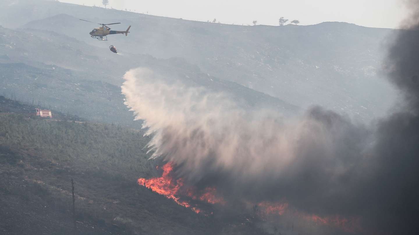 Um helicópetro combate as chamas durante o incêndio na encosta da aldeia de Moura da Serra, Arganil, 14 de agosto de 2025. De acordo com os dados disponíveis no ‘site’ da Autoridade Nacional de Emergência e Proteção Civil (ANEPC), quase 900 operacionais combatiam o fogo que deflagrou na quarta-feira na freguesia de Piódão, no concelho de Arganil, distrito de Coimbra, e se estendeu depois aos municípios de Oliveira do Hospital e Pampilhosa da Serra (Coimbra), e de Seia, já no distrito da Guarda. PAULO CUNHA/LUSA