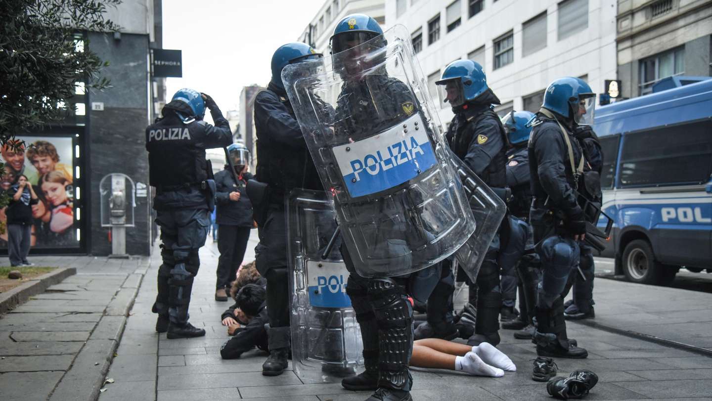 epa13314005 Italian police officers in riot gear stand around a person lying on the pavement during unrest near Piazza del Duomo in Milan, Italy, 18 October 2026. Clashes between protesters and police broke out during a demonstration against the rising cost of living on 17 October, followed by further disturbances in the city center on 18 October.  EPA/MATTEO CORNER