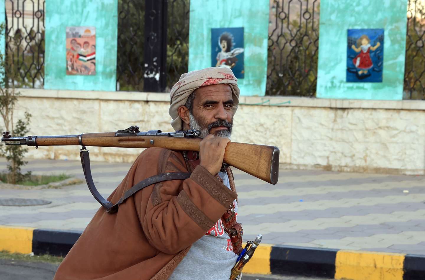 epa12616107 An armed man walks past paintings on display on a fence in Sana'a, Yemen, 28 December 2025. Yemen has been split by over 10 years of conflict, with the Houthis controlling large parts of the north while southern separatists have consolidated their grip in the south.  EPA/YAHYA ARHAB