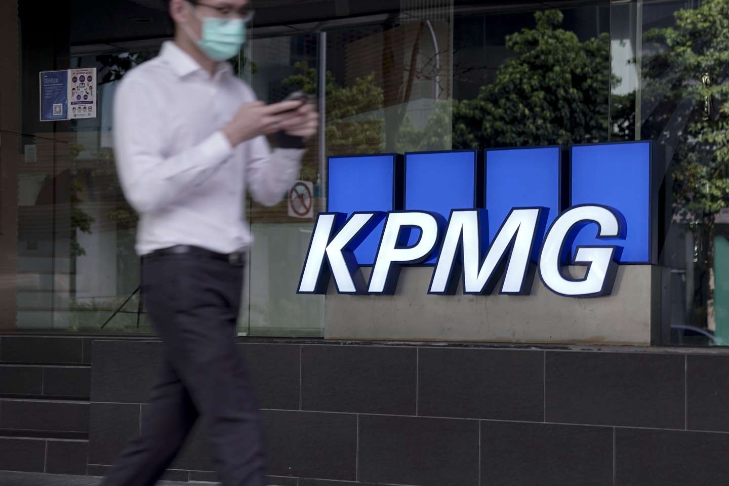 epa08777182 A man walks past the logo of auditing firm KPMG in the financial district in Singapore, 27 October 2020. The fallout of the global Covid-19 coronavirus pandemic has had a range of effects across workers from different sectors of the economy. As businesses gradually open up, economists are describing a 'K-shaped' recovery caused by lower wage workers affected by health and safety regulations, while white collar workers remain largely unaffected due to the advent of telecommuting and work from home arrangements.  EPA/WALLACE WOON
