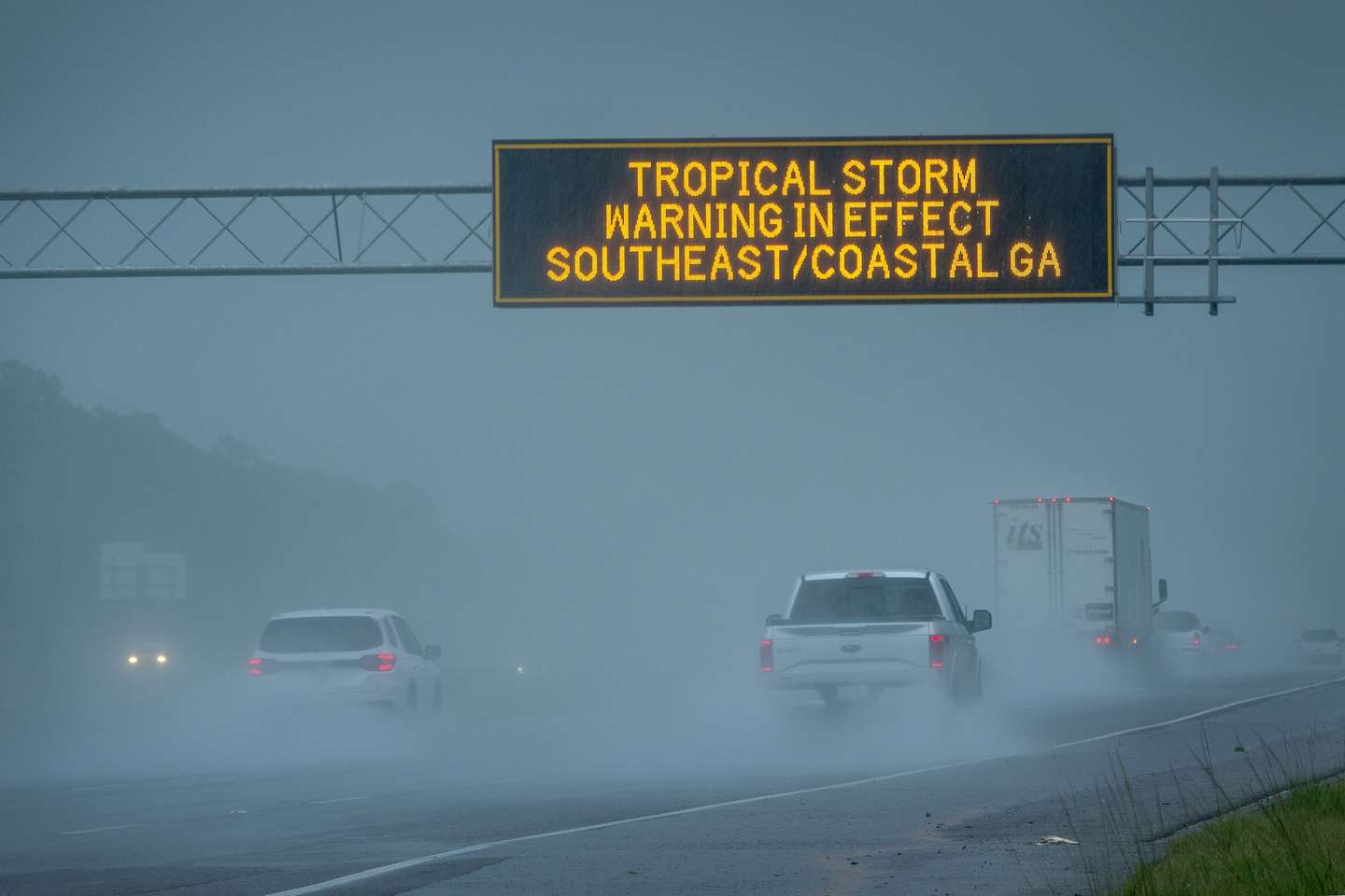 epa11529124 Vehicles pass under a tropical storm warning sign in effect due to tropical storm Debby in Waverly, Georgia, USA, 05 August 2024. Debby made landfall in Florida's Big Bend as a hurricane and is now a tropical storm that can produce potentially historic heavy rainfall across southeast Georgia, part of South Carolina and southeast North Carolina according to the National Hurricane Center.  EPA/CRISTOBAL HERRERA-ULASHKEVICH