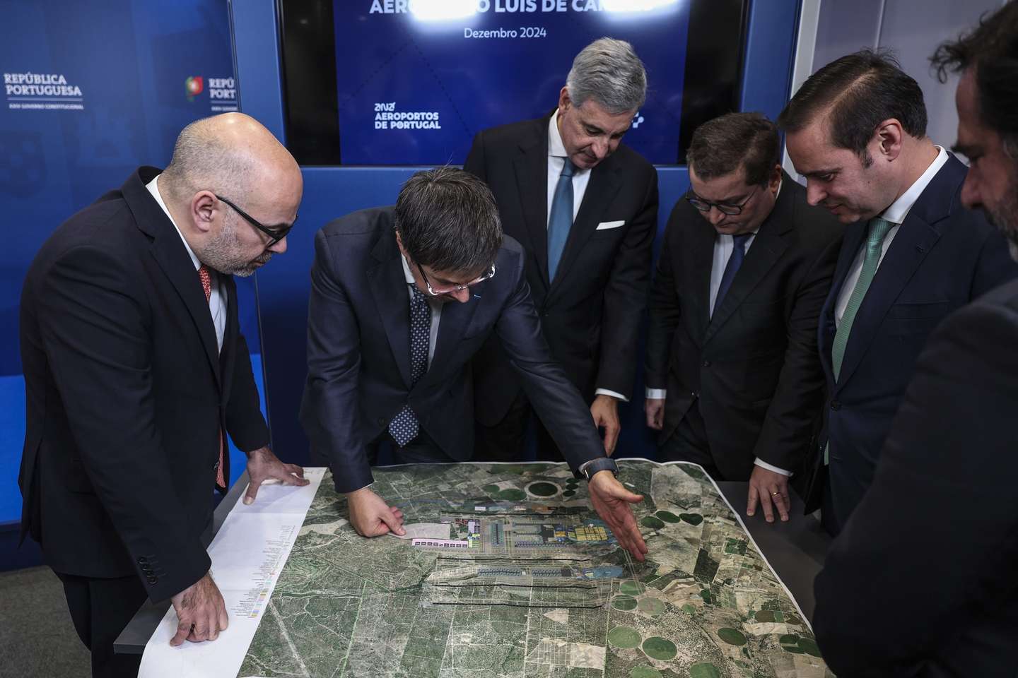O ministro das Infraestruturas e Habitação, Miguel Pinto Luz (E), o ministro de Estado e das Finanças, Joaquim Miranda Sarmento (3-D), o presidente da ANA, José Luis Arnaut (3-E), e o presidente executivo da ANA, Thierry Ligonnière (2-E), observam o plano do aeroporto após receberem o Relatório Inicial (High Level Assumption Report) da concessionária ANA sobre o desenvolvimento da capacidade aeroportuária de Lisboa,  para iniciar formalmente negociações sobre a extensão do contrato de concessão e viabilizar a construção do novo Aeroporto Luís de Camões, em Alcochete, 17 de dezembro de 2024.  ANDRÉ KOSTERS/LUSA