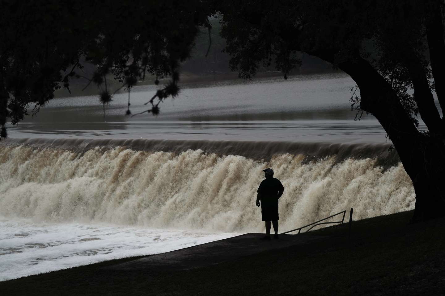 epa12219270 People watch the Guadalupe River flow over a dam, where the river measured 34.29 feet (10.5 meters) at its crest on 04 July, in Kerrville, Texas, USA, 05 July 2025. Early 04 July, floodwaters swept through a summer camp and nearby homes, killing at least two dozen people, with dozens of campers still unaccounted for.  EPA/DUSTIN SAFRANEK