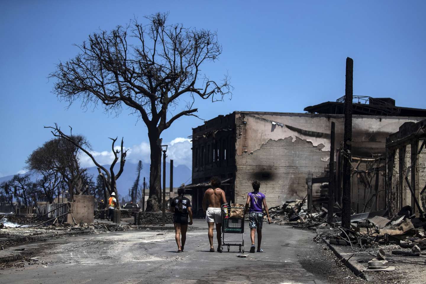 epaselect epa10796001 Residents push a kart amid the ruins left by a wild fire that swept through the city up to the shore and port in Lahaina, Hawaii, USA, 11 August 2023. At least 67 people were killed in the wildfires burning in Maui, which is considered the largest natural disaster in Hawaii's state history.  EPA/ETIENNE LAURENT