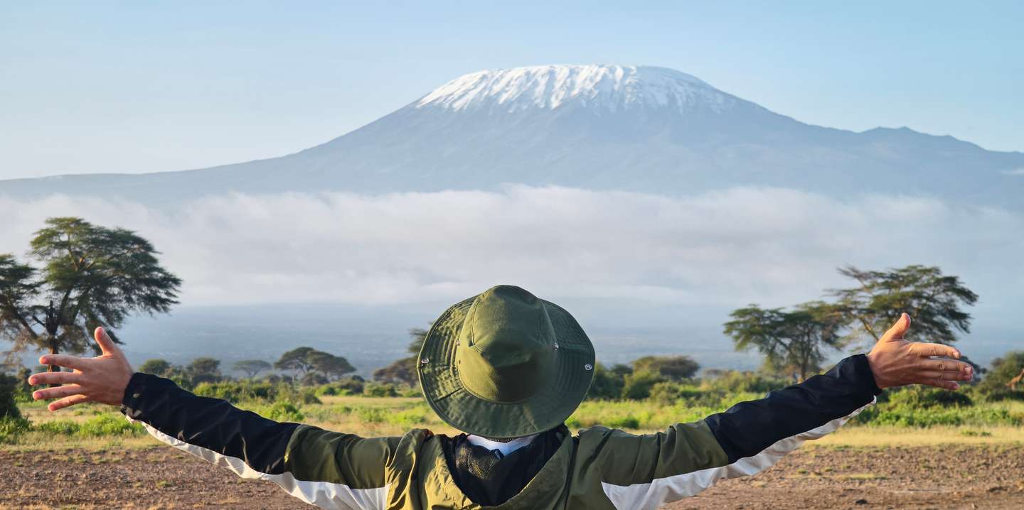 Homem de braços abertos com o Kilimanjaro ao fundo.