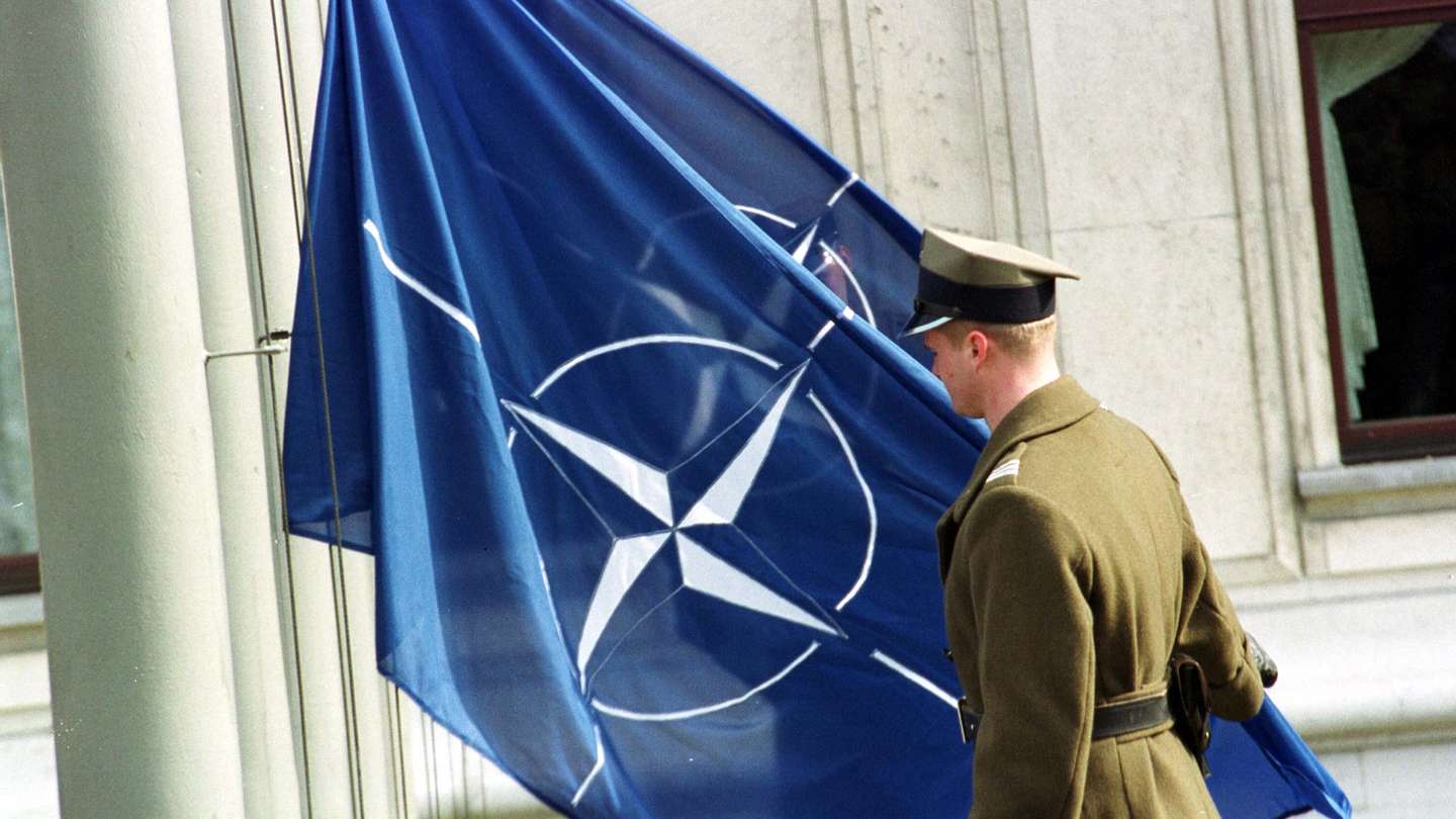 Polish Soldier Is Lifting Up A NATO Flag In Front Of The Polish Parliament Building As An Officia