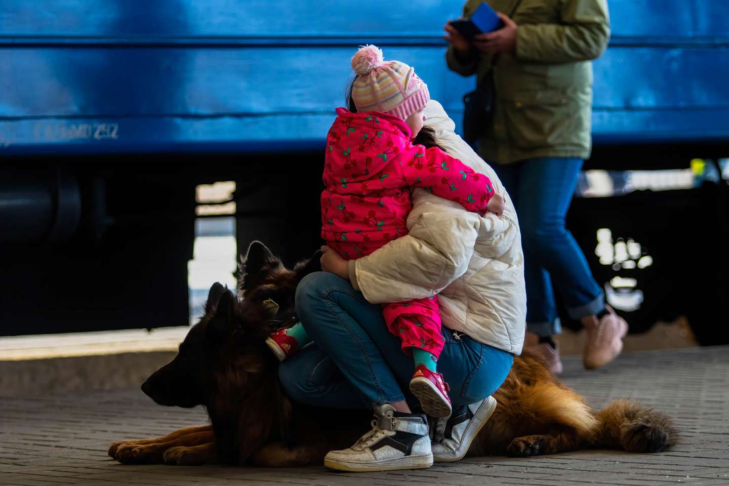 A woman holds a child and dogs on a train platform after