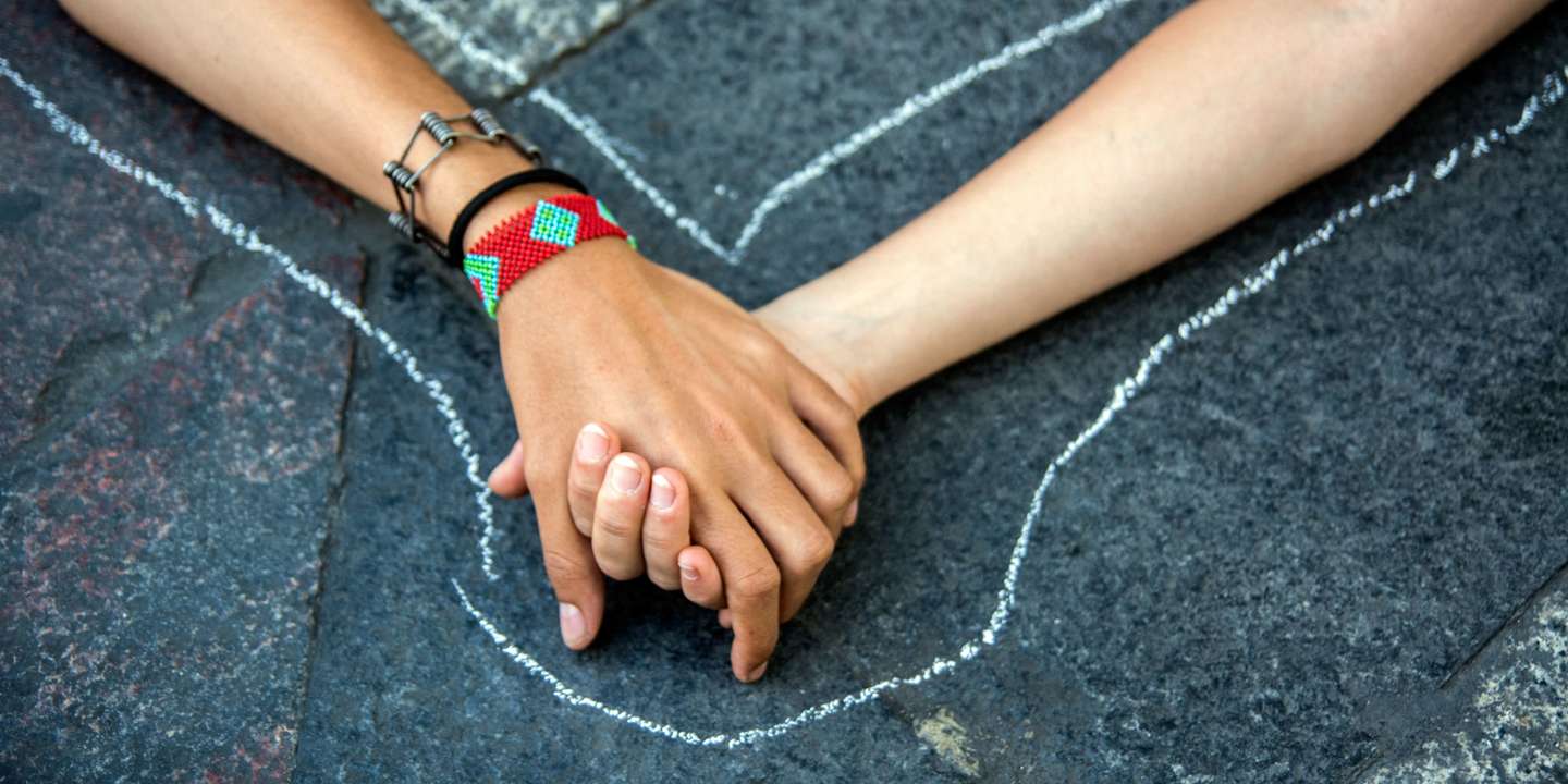 Two women holding hands on the floor as if they were dead