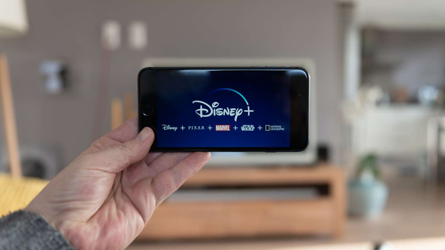 Disney+ startscreen on  mobile phone. Disney+ online video, content streaming subscription service. Man holds his smartphone up and looks at disney plus