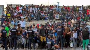 epa13150615 Police officers direct migrants at El Trampolin beach in Ceuta, Spain, 04 August 2026. According to Spanish officials, around 2,500 migrants remain in Ceuta following last week's massive border rush from Morocco, with many living in overcrowded reception centers or sleeping outdoors on beaches and in parks.  EPA/REDUAN