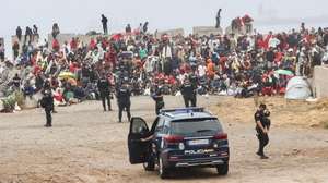 epa13182415 Several policemen stand guard near a group of migrants at El Trampolin beach in Ceuta, Spain, 21 August 2026. Authorities in Spain's North African enclave of Ceuta cleared migrants from El Trampolin beach for the second time on 21 August, grouping them in one area while crews cleaned the site. The Spanish government is providing temporary shelter for 1,800 migrants sleeping rough on Trampolin Beach and in the Loma Colmenar area of Ceuta, and plans to gradually expand these facilities.  EPA/REDUAN