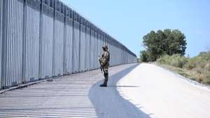 epa09440117 A soldier stands in front of a steel fence built along the Evros River in the area of Feres, at the Greek-Turkish border, Greece, 01 September 2021. The fence was built to prevent the illegal arrival of migrants into Greek territory.  EPA/DIMITRIS ALEXOUDIS
