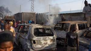 epa09567859 Sierra Leone residents of Freetown look at burned vehicles in the aftermath of an explosion at a junction outside Choithram Supermarket in Freetown, Sierra Leone, 06 November 2021.  At least 99 people have died following a massive fuel tanker explosion in the capital Freetown, after a fuel tanker collided with a truck.  EPA/MOHAMED KONNEH