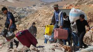 Refugiados sírios e libaneses que abandonam o Líbano, em fuga dos bombardeamentos intensivos de Israel contra o Hezbollah no sul do país e nos subúrbios de Beirute, fazem a travessia a pé, carregando malas pesadas, grandes sacos em serapilheira ou de supermercado,  crianças pequenas e bebés ao colo e idosos às cavalitas. Com sorte, conseguem um carro logo após as crateras, sem ela, resta-lhes carregar todo o peso e caminhar uns dois quilómetros até ao posto sírio desde fronteira de Massnaa, Líbano, 6 de outubro de 2024.  Duas crateras profundas marcam o local das explosões, a meio caminho entre os controlos fronteiriços dos dois países, deixando a via intransitável nos dois sentidos desde então, e que foram tão fortes que projetaram blocos em betão do separador central para as encostas a mais de 50 metros de distância. JOÃO RELVAS/LUSA
