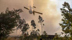 Um bombeiro protege-se da descarga de água um avião durante o combate ao incêndio florestal que desde a madrugada consome floresta em Mogueirães, Vouzela, 2 de julho de 2026. O Governo decretou situação de alerta, que vai vigorar das 00:00 de sexta-feira às 23:59 de segunda-feira, devido ao "significativo agravamento do risco de incêndios rurais". PAULO NOVAIS/LUSA