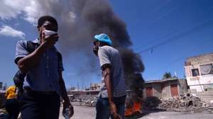 epaselect epa11922752 People walk near a burning tire during a new day of mobilizations against insecurity in the Tabarre area of Port-au-Prince, Haiti, 24 February 2024.  EPA/MENTOR DAVID LORENS