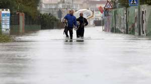 epa13315040 Two people and their dogs walk along a flooded street in Bellreguard, Valencia, Spain, 19 October 2026. Spain's State Meteorological Agency (Aemet) forecasts that the unsettled conditions caused by Storm Adam will persist across mainland Spain and the Balearic Islands, with very severe to torrential storms expected in the Valencian Community, along the southeastern coast and in the Balearic Islands.  EPA/Manuel Bruque