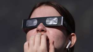 epa11996675 A woman uses protective glasses to watch a partial solar eclipse, at Greenwich Observatory in London, Britain, 29 March 2025. A solar eclipse happens when the Moon passes between the Sun and Earth, casting a shadow on Earth that either fully or partially blocks the Sun’s light in some areas.  EPA/NEIL HALL