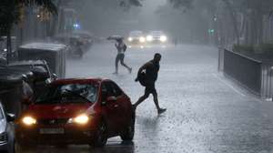 epa12234232 People cross a street during a rainfall in Barcelona, Catalonia, eastern Spain, 12 July 2025. Some 12 Spanish regions from northern and eastern Spain are on alert for heavy rainfalls.  EPA/Alberto Estevez