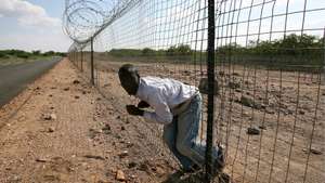 epa08306850 (FILE) An illegal immigrant struggles to climb through the electrified boarder fence between South Africa and Zimbabwe, Messina, South Africa, 18 April 2007 (reissued 19 March 2020). The South African government announced on 19 March 2020 that it would repair the fence at the Beitbridge border separating South Africa from Zimbabwe. The move comes after a pronouncement by President Cyril Ramaphosa that some of the country's ports, should be secured immediately .The fence stretches over 40 km, will now be repaired at a cost of R37 million and should be completed within a month.  EPA/KIM LUDBROOK