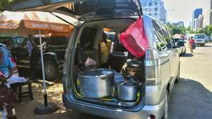 Um vendedor ambulante vende comida exposta na mala de um carro numa rua de Maputo, Moçambique, 28 de março de 2025. Chegam às primeiras horas do dia, estacionam o carro em locais centrais de Maputo e de mala aberta estes vendedores informais conseguem o sustento para a casa, servindo refeições na rua a preços de saldo. (ACOMPANHA TEXTO DA LUSA DO DIA 07 DE ABRIL DE 2025). LUÍSA NHANTUMBO/LUSA