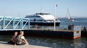 Um casal de turistas observa a chegada de um navio de passageiros, no Terreiro do Paço, em Lisboa, 10 de outubro de 2024. Cacilheiro. Catamarã. Transportes. Navio. Rio Tejo. Turismo. ANTÓNIO PEDRO SANTOS/LUSA