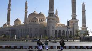 epa12621077 People walk past the Al-Shaab Mosque in Sana'a, Yemen, 01 January 2026. The Al-Shaab Mosque was constructed 17 years ago on an area of 27,300 square meters and accommodates 44,000 worshippers. It is the largest mosque in Yemen, featuring 23 domes of different sizes and six distinctive mud-brick minarets.  EPA/YAHYA ARHAB