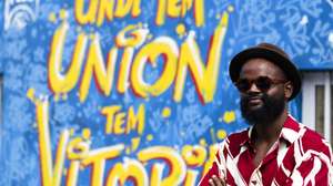 O artista plástico cabo-verdiano Hélder Cardoso, 33 anos, posa para a fotografia junto ao mural de sua autoria, em homenagem à participação da seleção cabo-verdiana de basquetebol no Mundial da modalidade, pintado exterior do pavilhão Gimnodesportivo Vavá Duarte, na Praia, Ilha de Santiago, Cabo Verde, 23 de novembro de 2023. O artista cabo-verdiano está prestes a celebrar uma década desde que optou pelas artes em vez da engenharia civil, numa carreira que lhe trouxe notoriedade e que, hoje, serve de “antídoto” contra as guerras. (ACOMPANHA TEXTO DA LUSA DO DIA 25 DE NOVEMBRO DE 2023). ELTON MONTEIRO/LUSA
