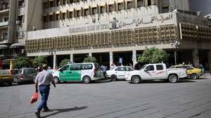 epa12098657 A person walks near the Commercial Bank of Syria building in Damascus, Syria, 14 May 2025. The value of the Syrian pound rose to about 8,000 per dollar after US President Donald Trump announced the lifting of sanctions on Syria during his visit to Riyadh, Saudi Arabia, for the Saudi-US Investment Forum.  EPA/MOHAMMED AL RIFAI