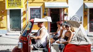 Um tuk-tuk transportando turistas passa por edifício com um cartaz com as palavras "Trânsito Caótico", da Associação QSintra -- Em Defesa de um Sítio Único, em Sintra, 16 de agosto de 2024. A Associação QSintra - Em Defesa de um Sítio Único - lançou uma iniciativa com faixas nas janelas e varandas e cartazes nas montras de lojas, restaurantes e cafés, exigindo à Câmara Municipal de Sintra medidas contra o "turismo de massas e caos no trânsito", com o objetivo de que a cidade não se transforme "num mero parque de diversões congestionado", pondo em causa o seu caráter de "sítio único". (ACOMPANHA TEXTO DA LUSA DO DIA 20 DE AGOSTO DE 2024). ANTÓNIO PEDRO SANTOS/LUSA