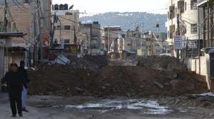 epa11963979 Palestinians walk near debris at a blocked road during an Israeli military operation in the West Bank city of Jenin, 14 March 2025. The Israeli military launched a military operation in Jenin and its camp on 21 January, resulting in at least 34 Palestinian deaths and dozens of injuries, according to the Palestinian Ministry of Health.  EPA/ALAA BADARNEH