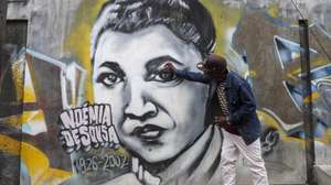 O artista moçambicano Bruno Mateus, conhecido como Shot.B, posa junto ao mural dedicado à Noémia de Sousa no bairro da Mafalala, em Maputo, Moçambique, 31 de agosto de 2026. Cem anos após ter nascido, nem o mural com o rosto aviva a memória dos residentes da Mafalala, em Maputo, onde a poeta e jornalista Noémia de Sousa cresceu, entre pedidos de iniciativas para manter vivo o legado. (ACOMPANHA TEXTO DA LUSA DO DIA 31 DE AGOSTO DE 2026). LINA CEBOLA/LUSA.