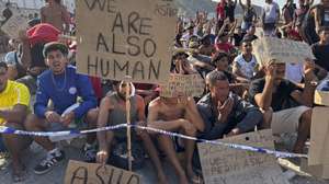 epa13176333 Migrants hold signs that read 'We are also human' and 'Asylum' during a hunger strike at the El Trampolin beach campsite in Ceuta, Spain, 17 August 2026. The migrants entered the Spanish enclave from Morocco during the mass border crossings that began on 30 July.  EPA/LAURA RINCON