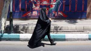epa13055973 A veiled Iranian woman walks past an anti-US mural (depicting an Iranian and US negotiation table) next to the former US embassy in Tehran, Iran, 22 June 2026. Leaders of the Iranian negotiation team, Mohammad Bagher Ghalibaf and Abbas Araghchi, left the Lucerne Summit in Switzerland after 18 hours of talks with the US, Pakistan, and Qatar.  EPA/ABEDIN TAHERKENAREH RESTRICTIONS: NO Access Israel Media/Persian Language TV Stations Outside Iran/Strictly No Access BBC Persian/VOA Persian/Manoto TV/Iran International TV. (As mandated by Iran's Directorate General for Foreign Media) --