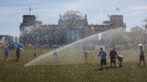 epa13060558 People are seen behind water bubbles as they move between sprinklers in front of the Reichstag building, the seat of the German parliament, during hot temperatures in Berlin, Germany, 24 June 2026. The German Weather Service forecasted strong to extreme heat stress in large parts of the country.  EPA/CLEMENS BILAN