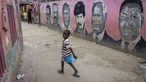 Uma criança passa em frente do mural que junta políticos como Neto (E) e Savimbi (2-E), durante uma reportagem da agência Lusa no bairro do Sambizanga, dias após da visita do Papa Leão XIV a Angola, em Luanda, Angola, 22 de abril de 2026. No Sambizanga, bairro de Nagrelha e Bangão, Mantorras e William Carvalho, Dádiva pousa na rua cor-de-rosa, a do mural que junta políticos como Neto e Savimbi, na Luanda dos contrastes, onde a pobreza se esconde atrás dos arranha-céus e se mostra sem vergonha nos musseques. (ACOMPANHA TEXTO DA LUSA DO DIA 27 DE ABRIL DE 2026). JOSÉ SENA GOULÃO/LUSA