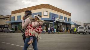 epa09604355 A masked woman carrying a child walks through the streets of the rural town of Parys, South Africa, 26 November 2021. The South African Department of Health and scientists from the Network for Genomic Surveillance revealed details of a newly detected and highly mutated Covid-19 variant, B.1.1.529 which immediately led to Japan, Israel and the European Union placing stricter measures against South Africans travelling to and from their part of the world.  EPA/KIM LUDBROOK