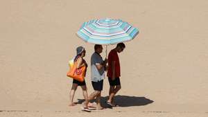Turistas protegem-se do sol com um guarda-sol numa praia em Albufeira, 22 de agosto de 2023. Por causa do tempo quente, o IPMA colocou os distritos de Vila Real, Bragança, Viseu, Guarda, Coimbra, Castelo Branco e Santarém sob aviso vermelho entre as 00:00 de hoje e as 10:00 de quinta-feira. LUÍS FORRA/LUSA