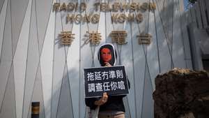 epa08970328 A Radio Television Hong Kong, RTHK, journalist dons a mask representing their colleague Nabel Qoser during a protest outside her office in Kowloon Tong, Hong Kong, China, 28 January 2021. RTHK journalists came out to support their colleague Qoser who has had her civil service contract terminated after her tough questioning of government officials, including Chief Executive Carrie Lam, during the 2019 protests. Instead of a civil service contract she has been offered a 120-day contract as an internal investigation into complaints made about her reporting continues.  EPA/JEROME FAVRE