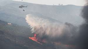 Um helicópetro combate as chamas durante o incêndio na encosta da aldeia de Moura da Serra, Arganil, 14 de agosto de 2025. De acordo com os dados disponíveis no ‘site’ da Autoridade Nacional de Emergência e Proteção Civil (ANEPC), quase 900 operacionais combatiam o fogo que deflagrou na quarta-feira na freguesia de Piódão, no concelho de Arganil, distrito de Coimbra, e se estendeu depois aos municípios de Oliveira do Hospital e Pampilhosa da Serra (Coimbra), e de Seia, já no distrito da Guarda. PAULO CUNHA/LUSA