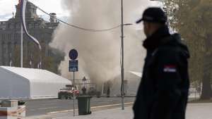 epa12472278 Police officers secure the scene in front of the Parliament building as smoke billows from a tent, in Belgrade, Serbia, 22 October 2025. A man was seriously injured in a shooting incident outside the parliament building, near a tent of supporters of President Vucic, who described the incident as a 'terrorist act.' One person was detained in connection with the shooting.  EPA/STRINGER