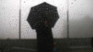 epa12606661 A man holding an umbrella is seen through a car window during rain and fog on the outskirts of Srinagar, the summer capital of Indian Kashmir, 21 December 2025. Kashmir witnessed an end to a prolonged dry spell, with the upper reaches witnessing light to heavy snowfall and the plains witnessing intermittent rains on the day marking the onset of Chillai Kalan, the harshest 40-day winter spell. Meteorological Department officials have forecast ongoing precipitation and colder temperatures as the valley braces for deeper winter conditions.  EPA/FAROOQ KHAN