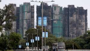 epa12576299 Traffic passes the charred buildings of Wang Fuk Court and promotional banners near a polling station in Tai Po district during the Legislative Council General Election in Hong Kong, China, 07 December 2025. Hong Kong's 'patriots-only' Legislative Council election is being held on 07 December as the city mourns the Wang Fuk Court fire in Tai Po, one of Hong Kong's deadliest fires in decades, with public calls for accountability amid a widening probe into the tragedy.  EPA/MAY JAMES