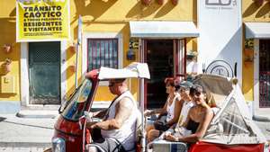 Um tuk-tuk transportando turistas passa por edifício com um cartaz com as palavras "Trânsito Caótico", da Associação QSintra -- Em Defesa de um Sítio Único, em Sintra, 16 de agosto de 2024. A Associação QSintra - Em Defesa de um Sítio Único - lançou uma iniciativa com faixas nas janelas e varandas e cartazes nas montras de lojas, restaurantes e cafés, exigindo à Câmara Municipal de Sintra medidas contra o "turismo de massas e caos no trânsito", com o objetivo de que a cidade não se transforme "num mero parque de diversões congestionado", pondo em causa o seu caráter de "sítio único". (ACOMPANHA TEXTO DA LUSA DO DIA 20 DE AGOSTO DE 2024). ANTÓNIO PEDRO SANTOS/LUSA